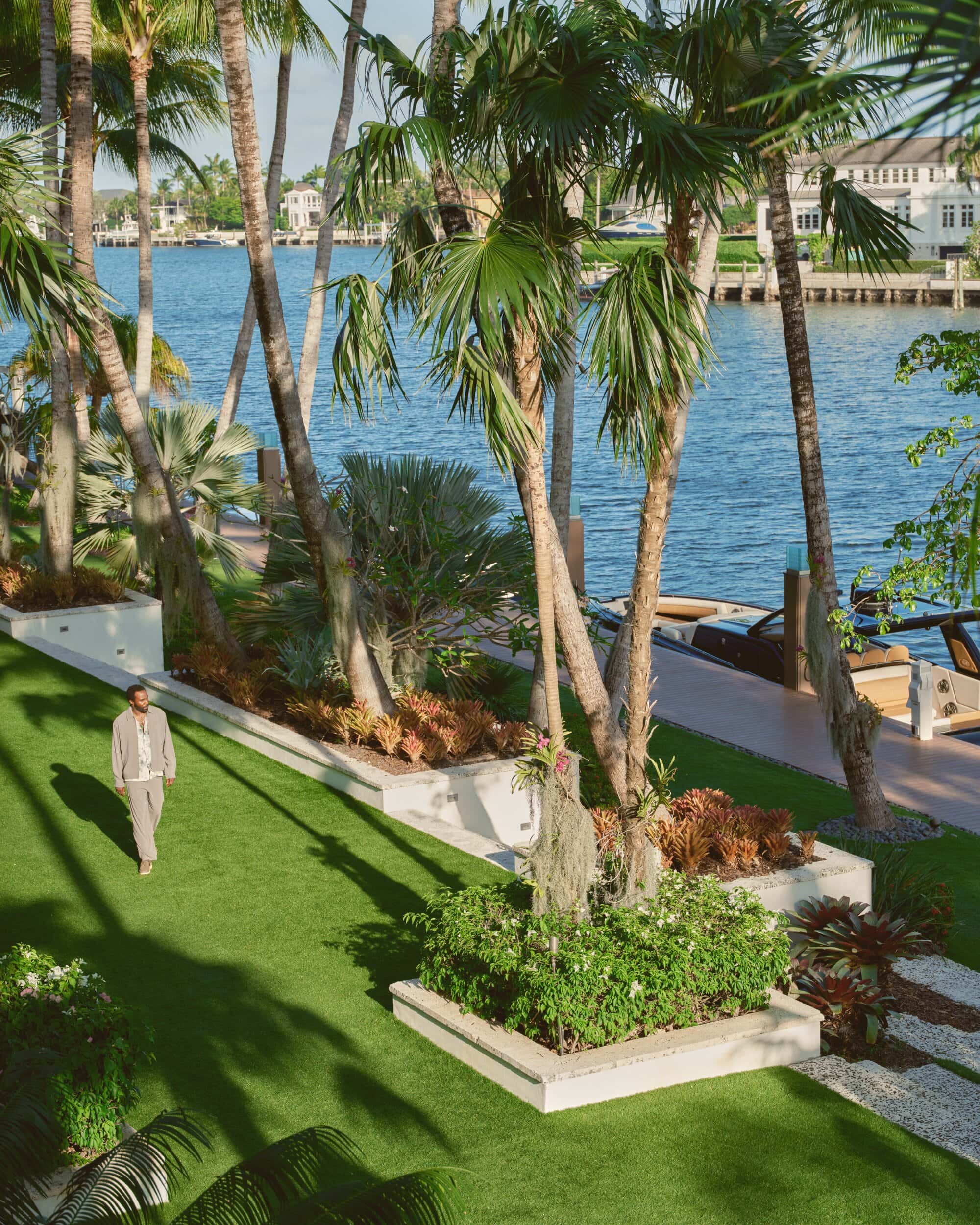 Tramell Tillman walking across a manicured lawn lined with palm trees along a waterfront for Kith Spring 2025 ad campaign.
