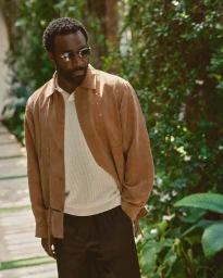 Tramell Tillman wearing brown suede shirt and sunglasses outdoors for Kith Spring 2025 ad campaign.