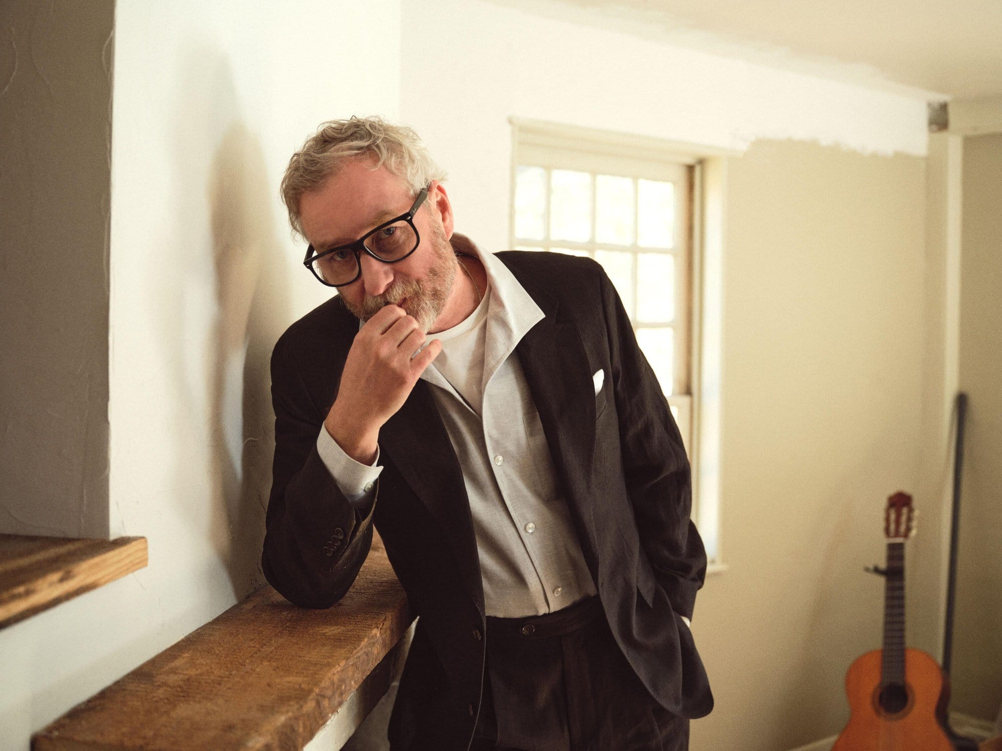 Matt Berninger wearing a dark blazer leaning against a wooden mantelpiece for Todd Snyder Spring 2025 campaign.