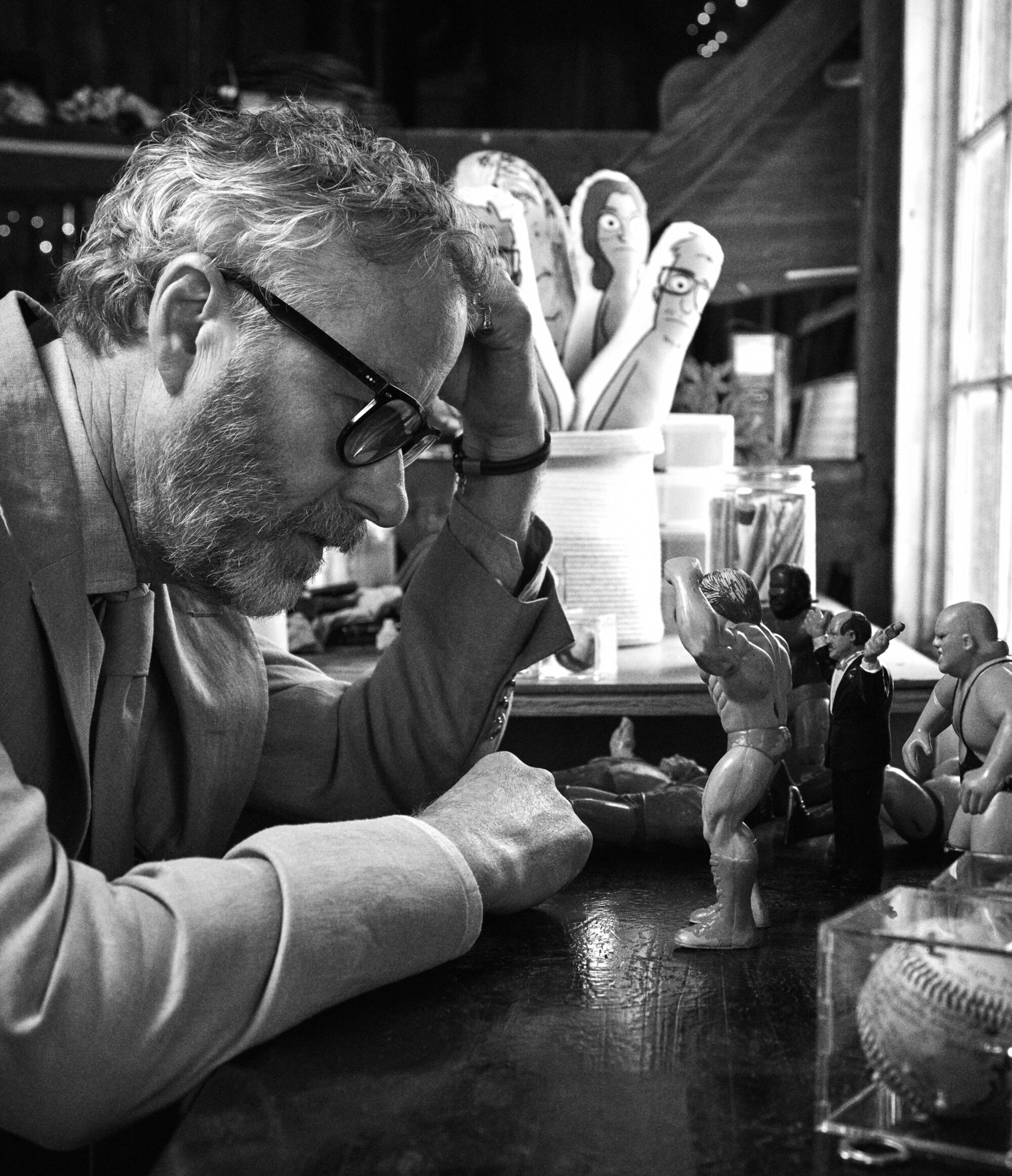 Matt Berninger in glasses and suit jacket looking down at small vintage wrestling action figures on a table