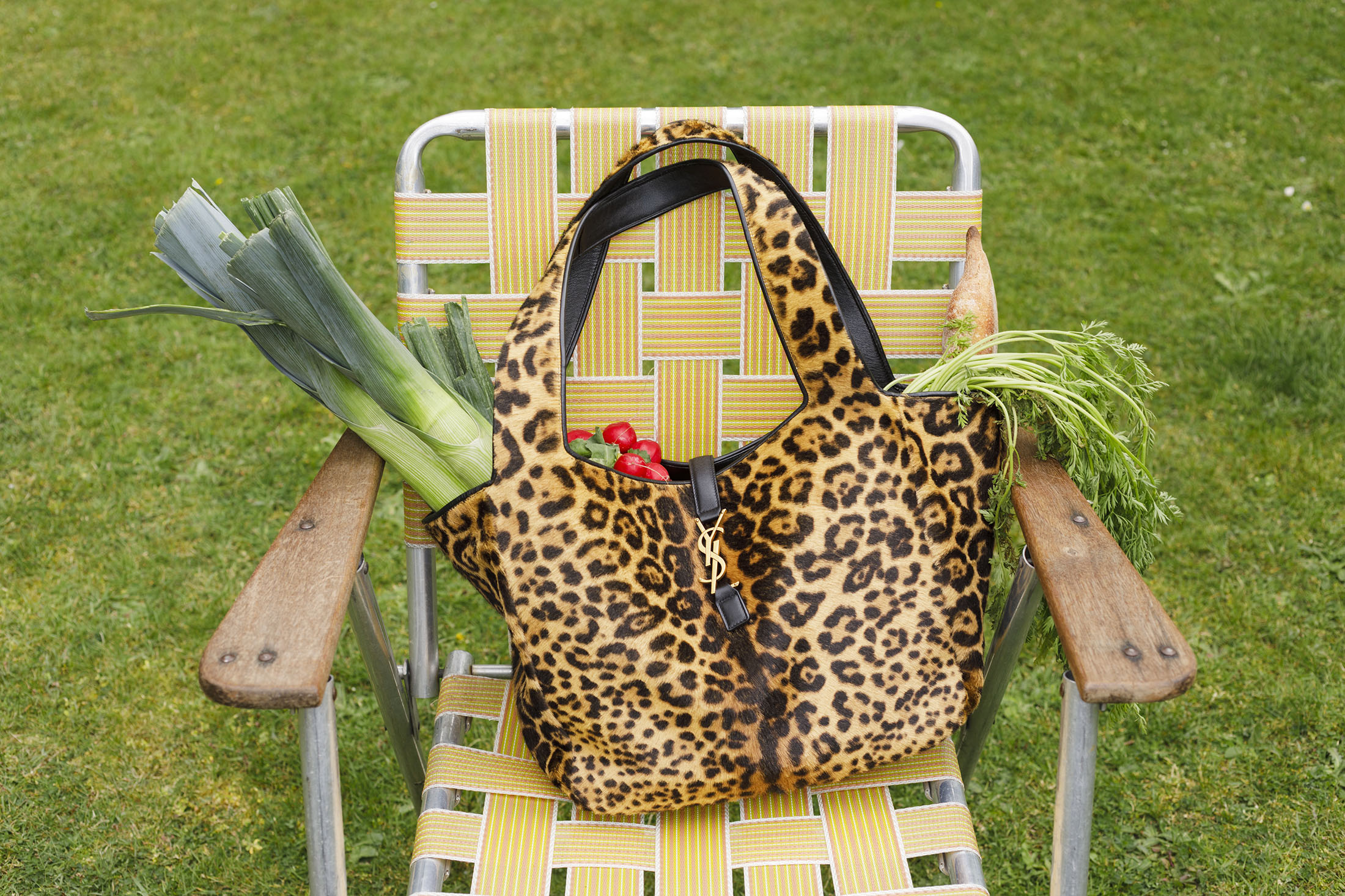 Leopard print handbag with vegetables resting on a yellow webbed lawn chair over grass