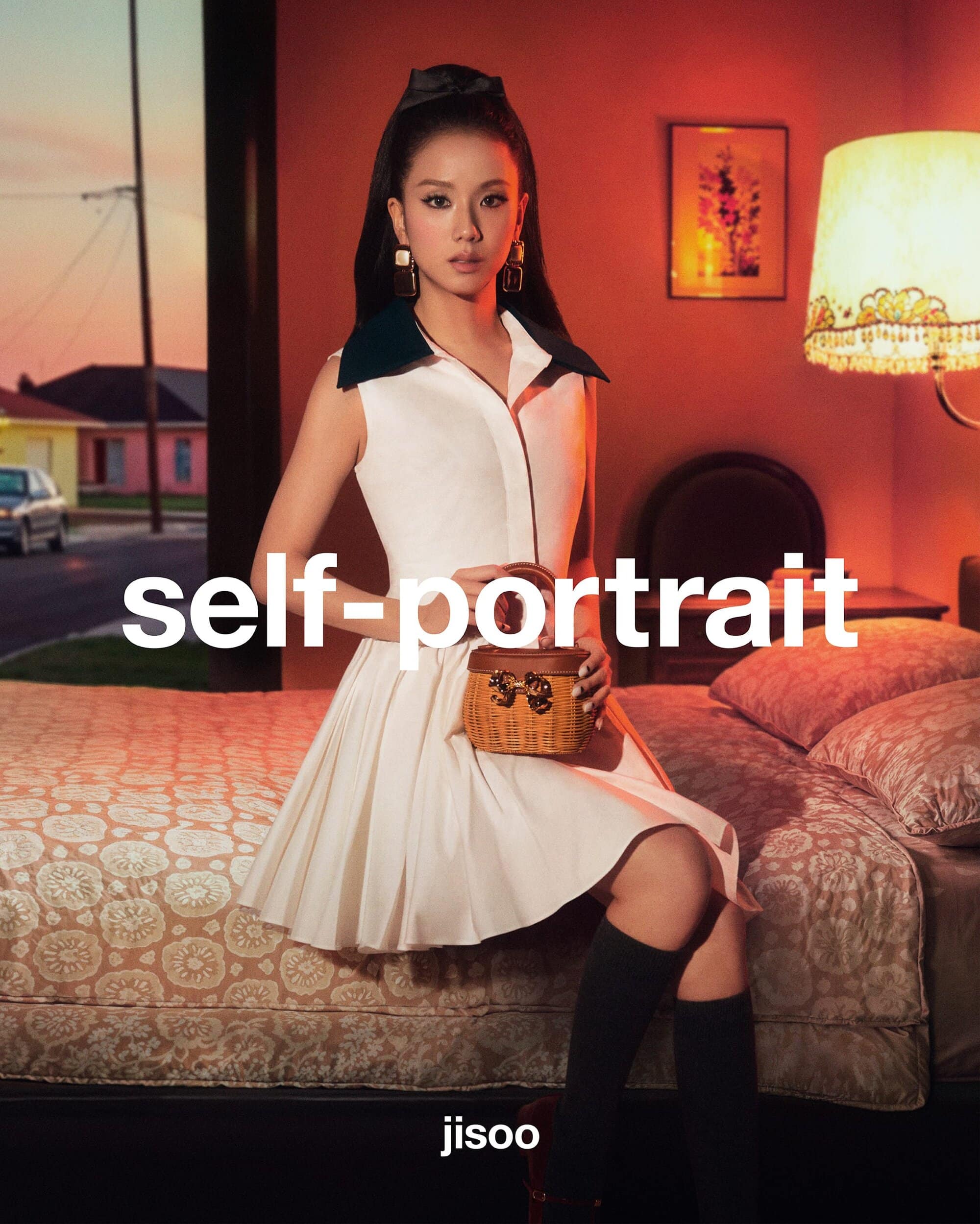 Jisoo seated on a bed in a hotel room wearing a white dress and holding a small woven handbag for Self-Portrait.