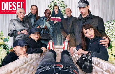 Group of diverse people standing around an open casket holding a person wearing denim jeans and a red belt for a Diesel ad campaign.