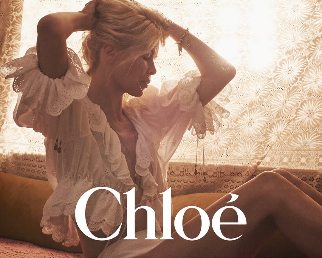 Claudia Schiffer posing in a white embroidered eyelet blouse against a lace curtain backdrop for Chloe