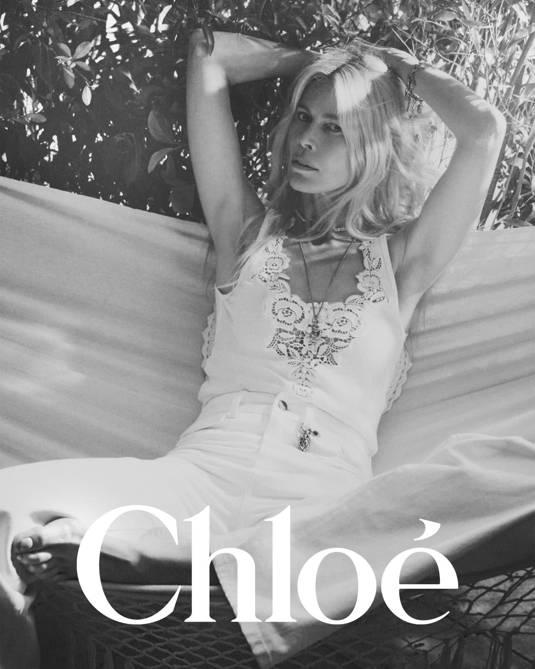 Claudia Schiffer resting in a hammock wearing a white lace tank top and trousers for Chloé High Summer 2025 campaign.
