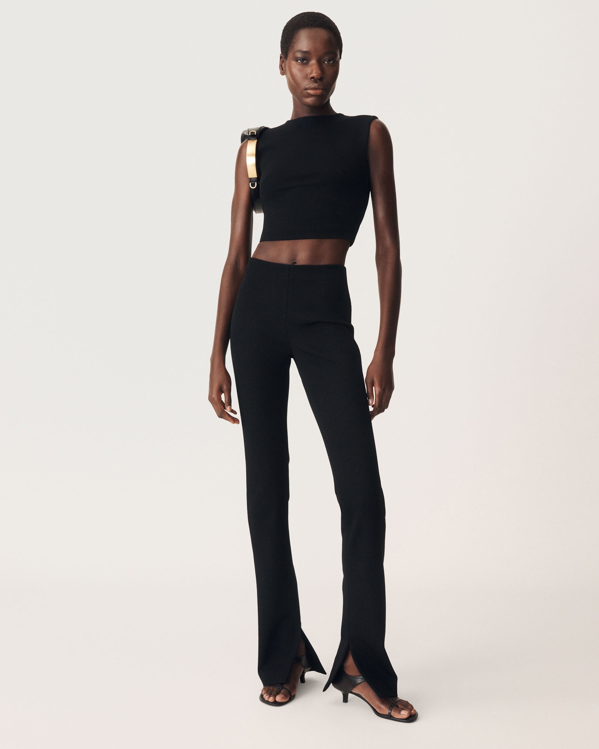 Model in black sleeveless top and flared trousers standing against white seamless background for Zara 50 Years 50 Icons campaign