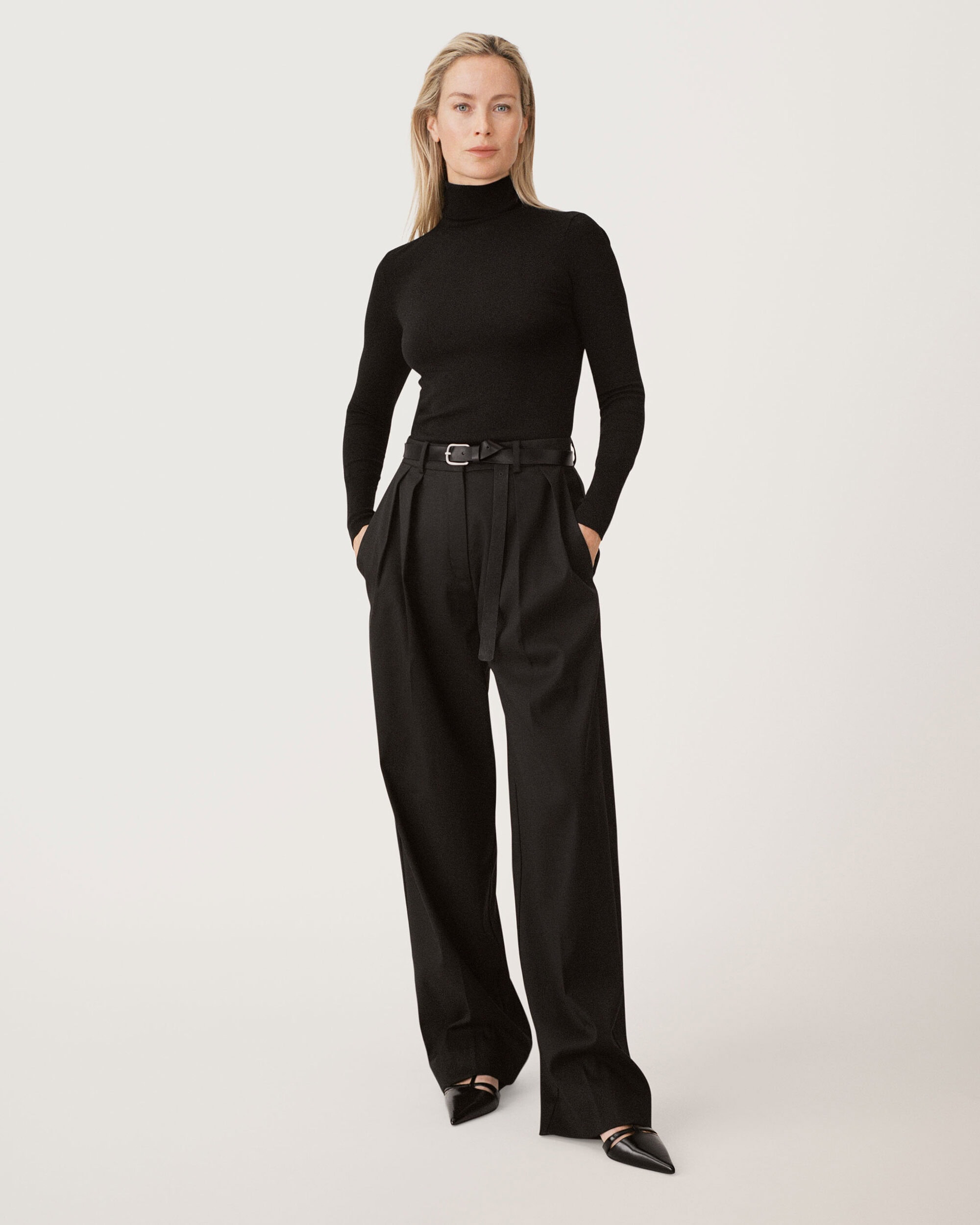 Model in black turtleneck and pleated trousers standing against a seamless white studio background for Zara 50 Years 50 Icons campaign.