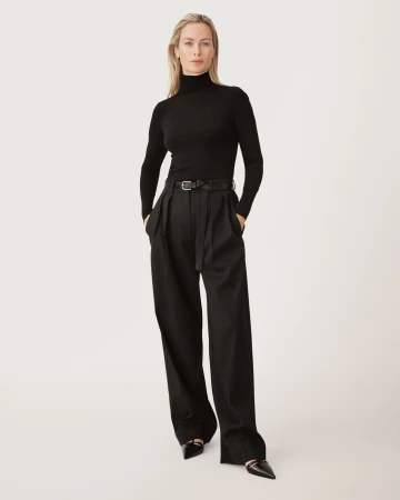 Model in black turtleneck and pleated trousers standing against a seamless white studio background for Zara 50 Years 50 Icons campaign.