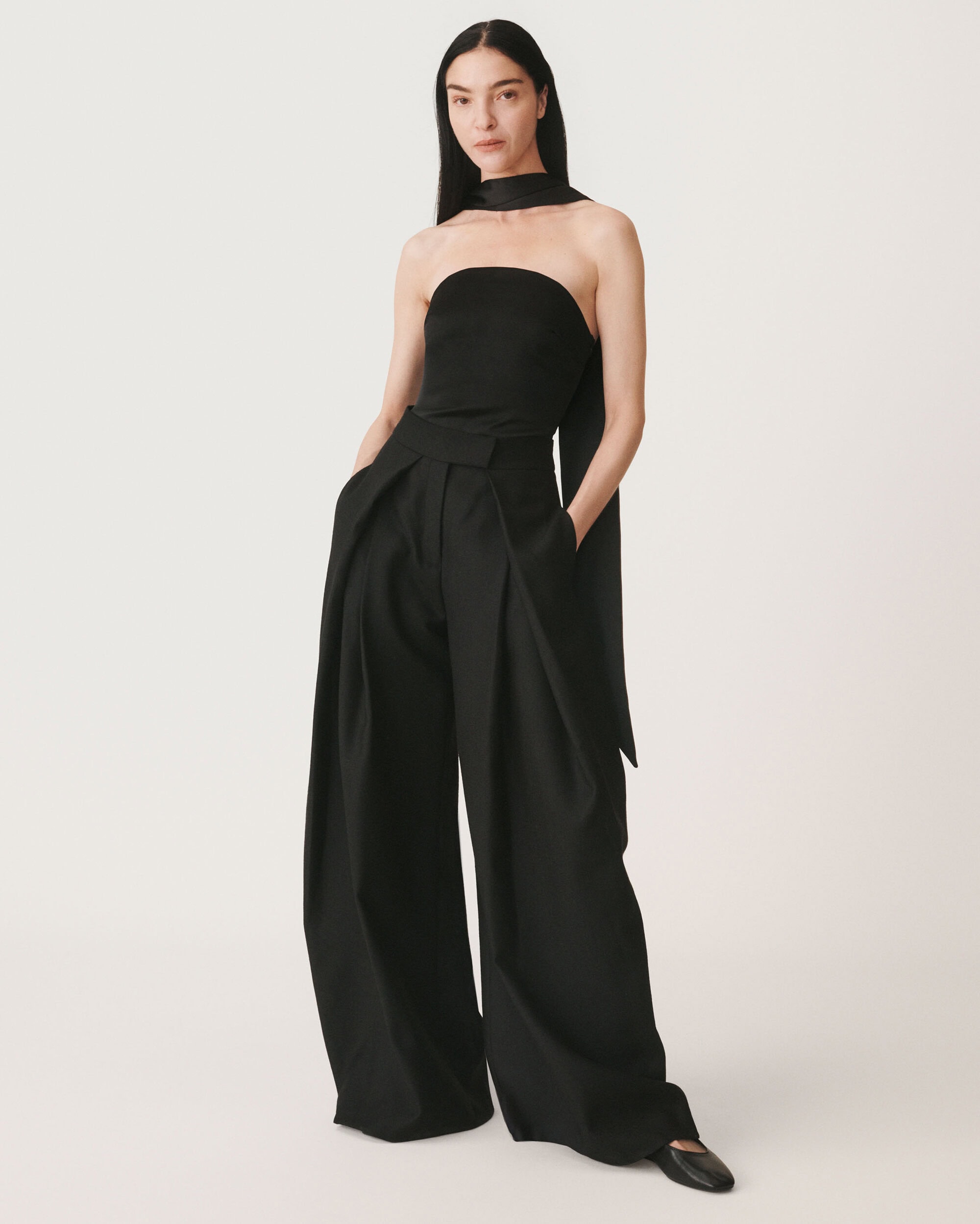 Model in black strapless top and wide leg trousers standing against a seamless white background