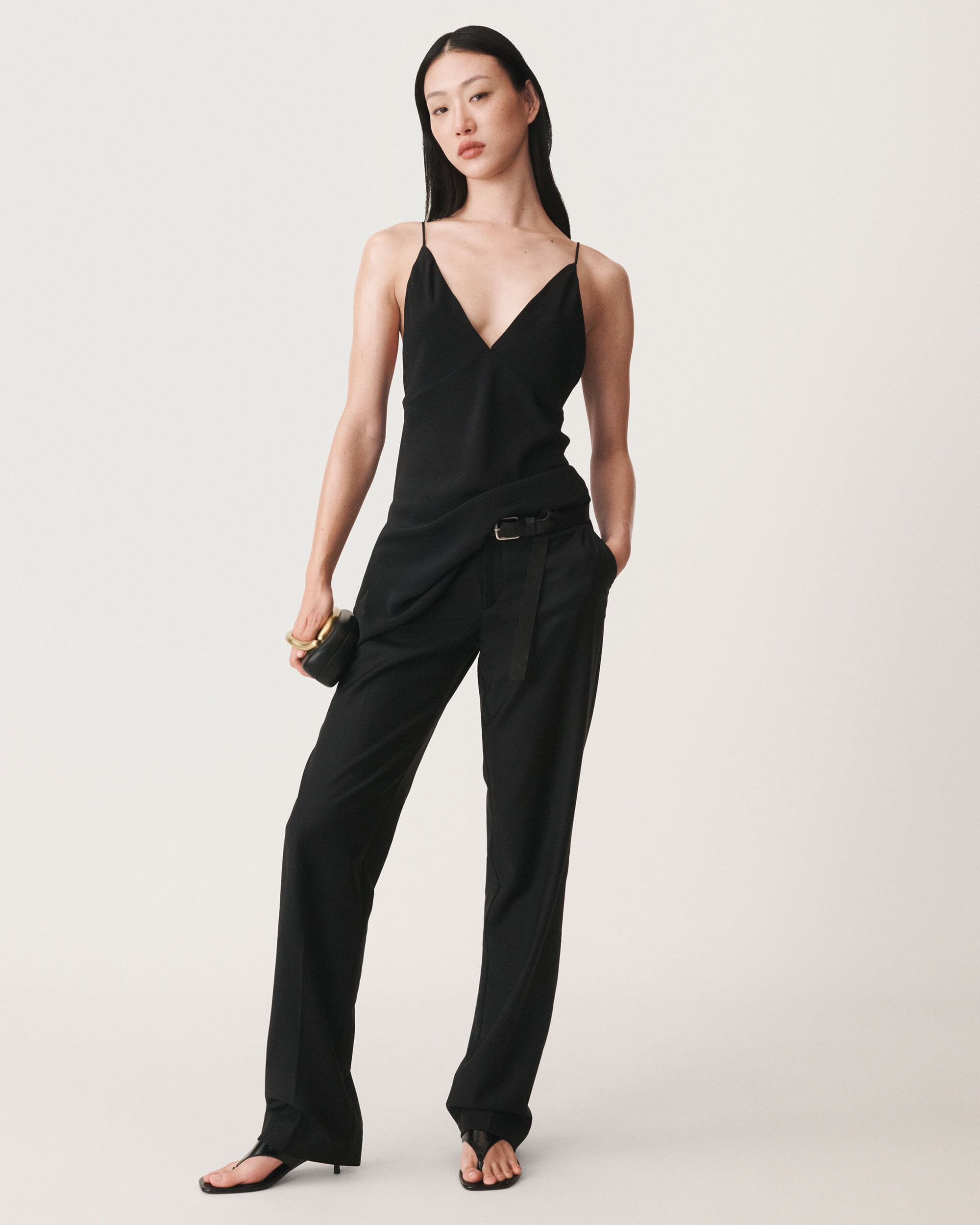 Asian female model wearing a black slip top and trousers holding a clutch against a white background for Zara campaign