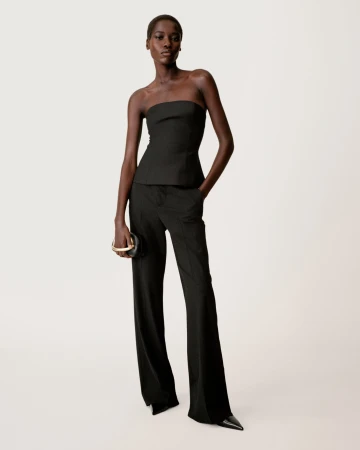 Model in a black strapless top and trousers holding a round black handbag against a light seamless background
