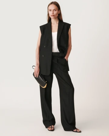 Model wearing a black vest and trousers holding a black clutch against a plain white background