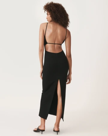 Model wearing a black backless dress and black sandals against a white backdrop