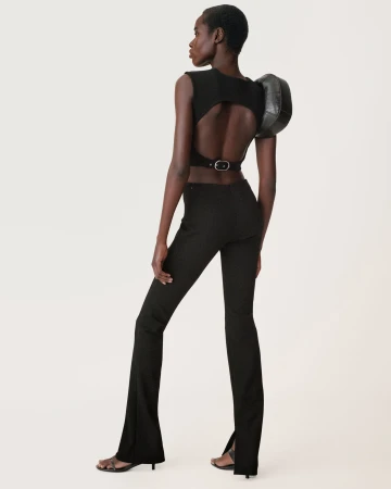 Black model wearing an open-back black crop top and flared trousers against a seamless white background.