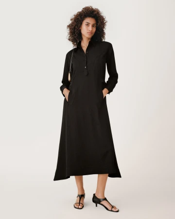 Model wearing a long black button-down dress and black sandals against a solid white background