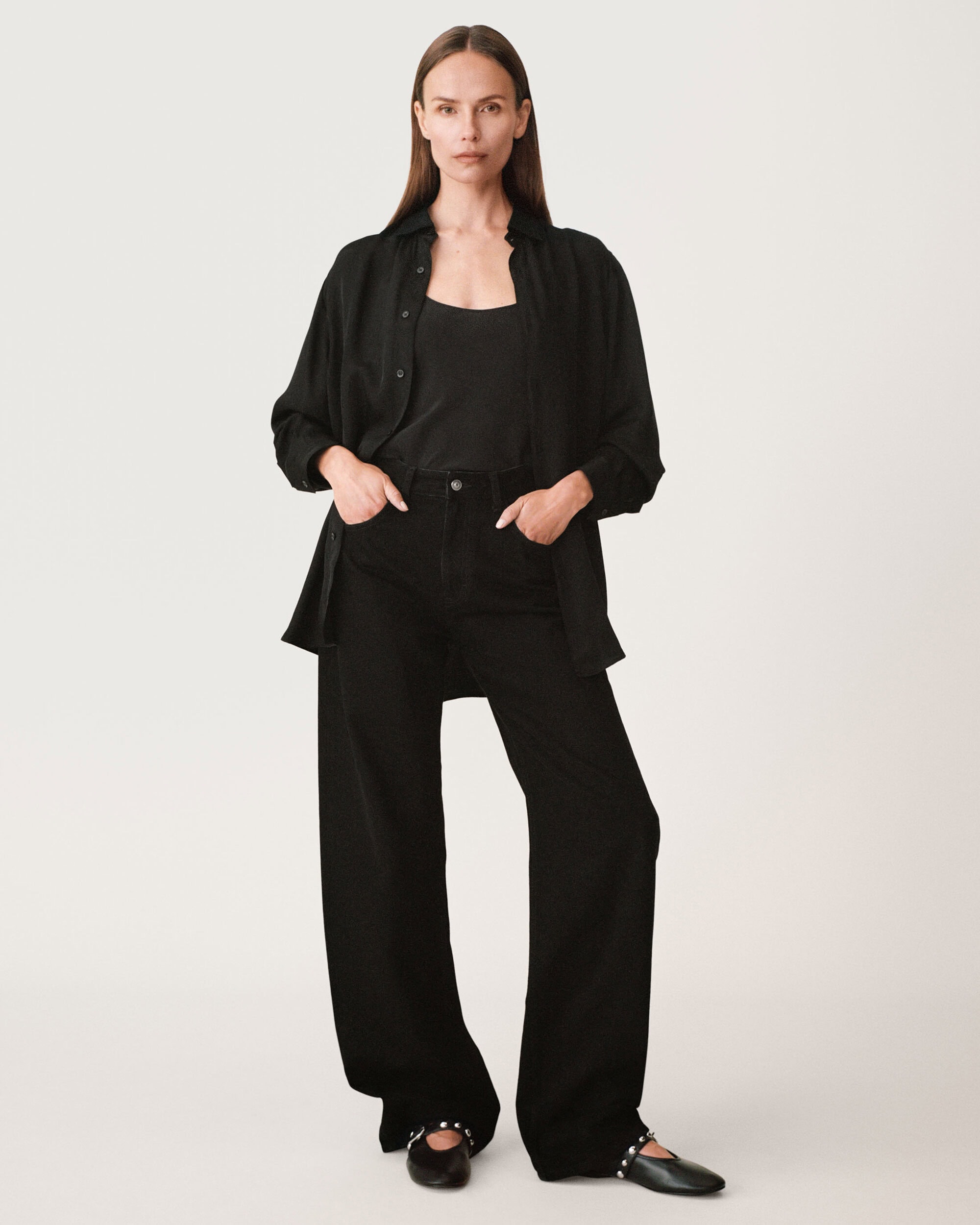 Model wearing black shirt and trousers with hands in pockets against a plain white background