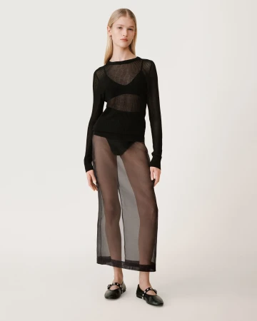 Model standing on white studio floor wearing a sheer black knit top and long translucent skirt with black flats