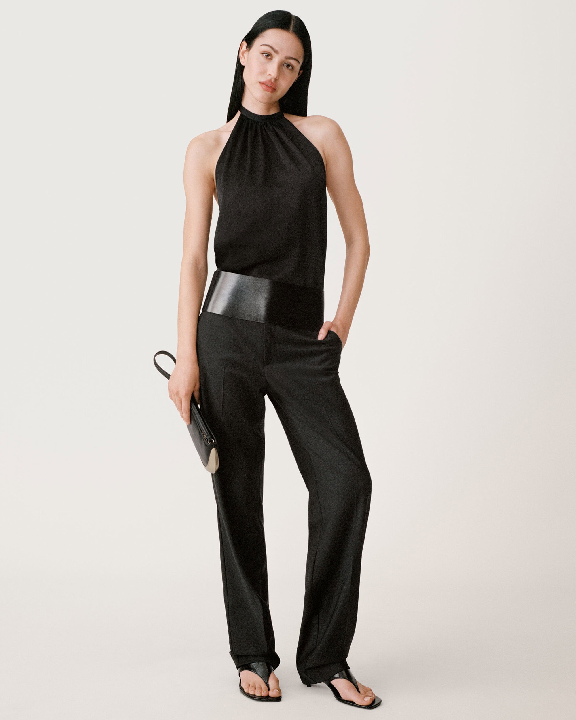 Model in a black halter top and black trousers against a neutral white background