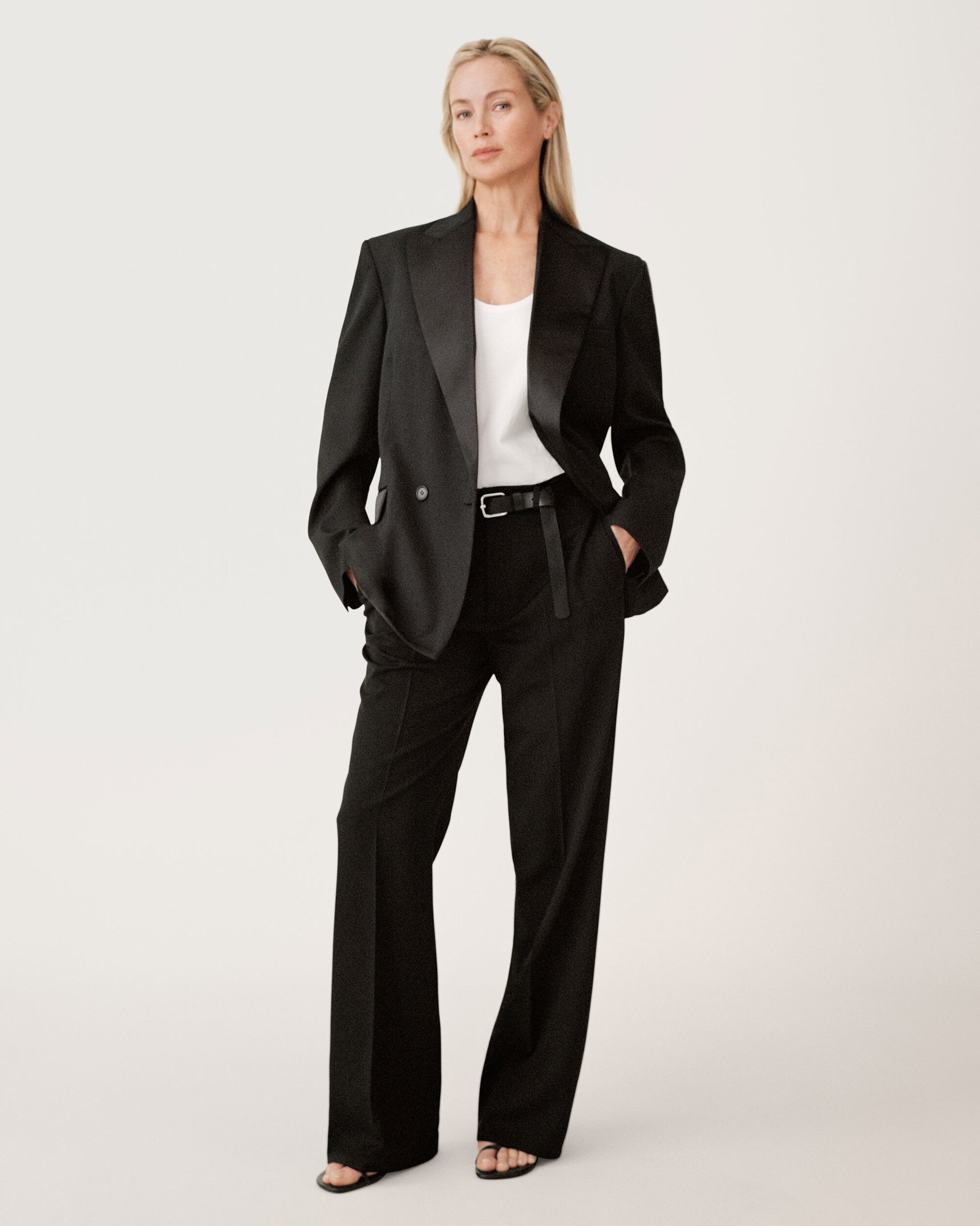 Model standing against a white seamless backdrop wearing a black blazer and trousers with a white top