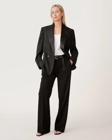 Model standing against a white seamless backdrop wearing a black blazer and trousers with a white top