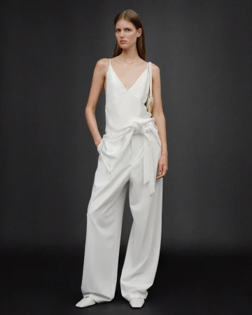 Model wearing a white slip top and matching wide-leg trousers against a dark textured background for Zara.