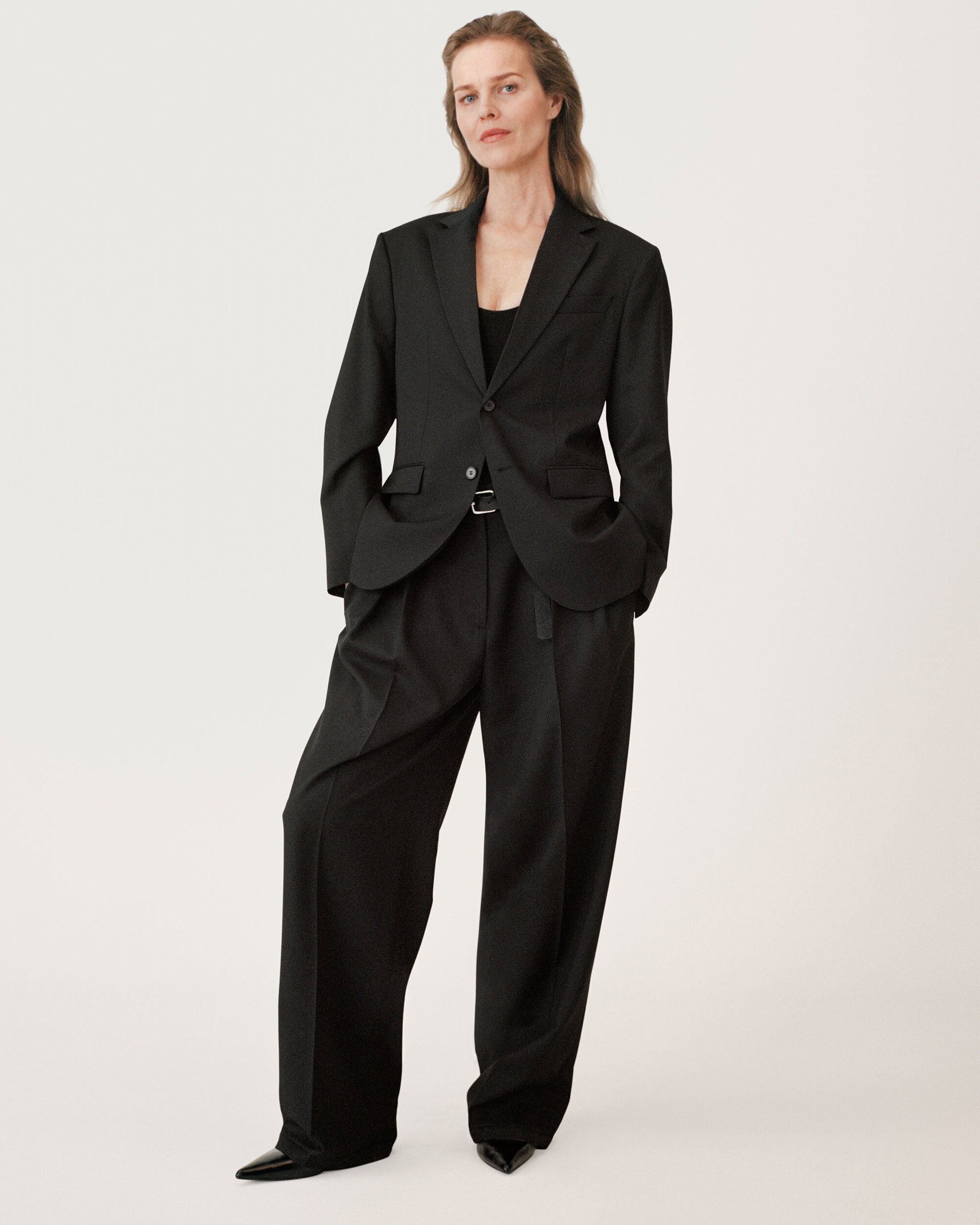 Model wearing a black blazer and matching trousers standing against a seamless white background