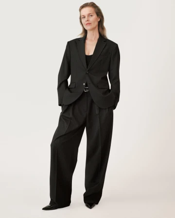 Model wearing a black blazer and matching trousers standing against a seamless white background