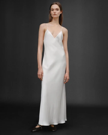 Model wearing a long white slip dress against a dark grey seamless studio backdrop