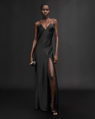 Black model in a long black silk slip dress holding a clutch against a dark backdrop for Zara 50 Years 50 Icons campaign.