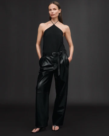 Model wearing a black halter top and black trousers posing against a dark studio background for Zara.
