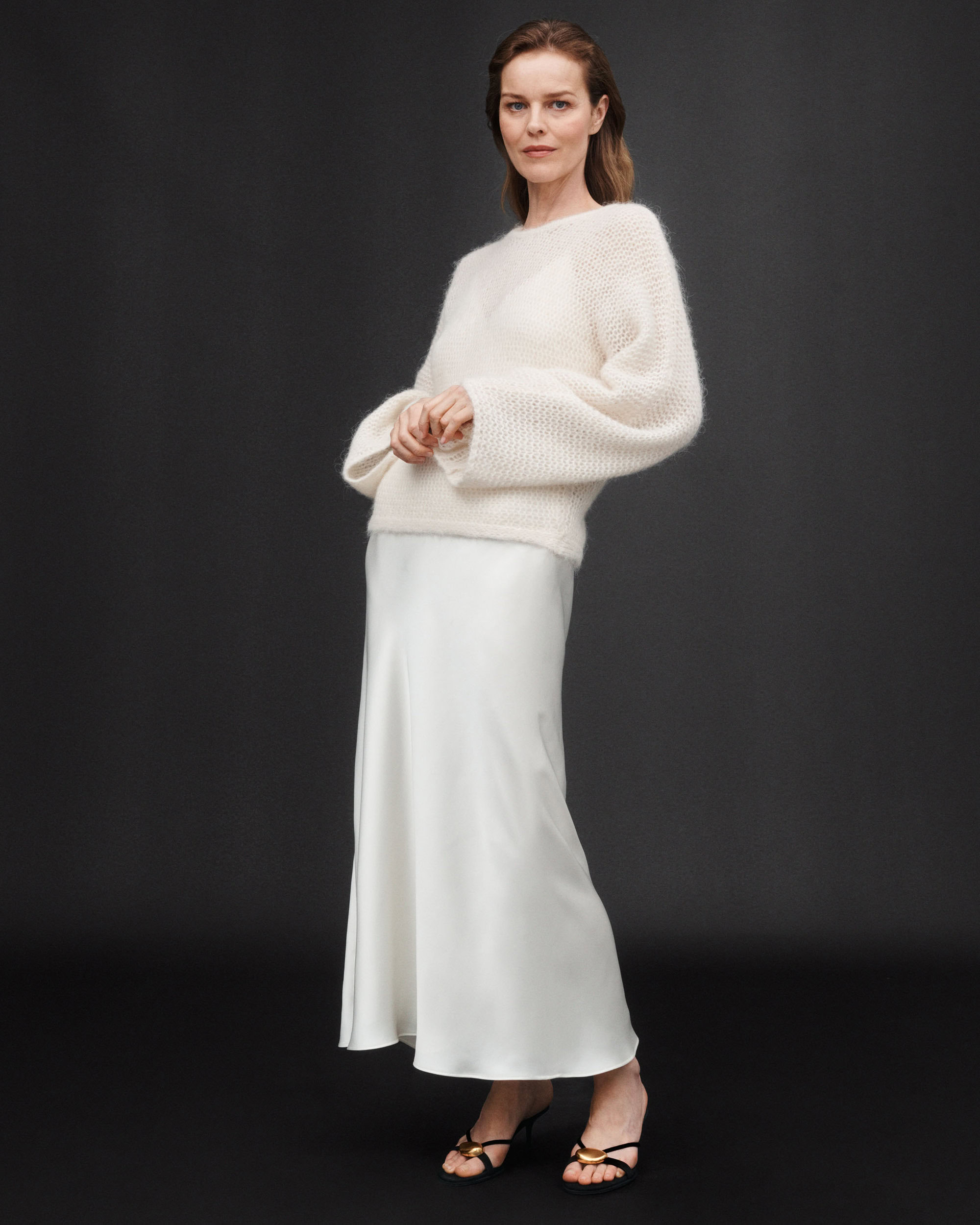 Model wearing a fluffy white knit sweater and a long satin skirt against a dark background for Zara