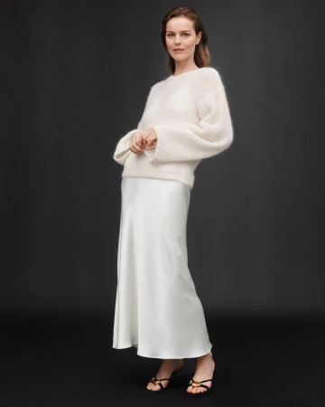Model wearing a fluffy white knit sweater and a long satin skirt against a dark background for Zara