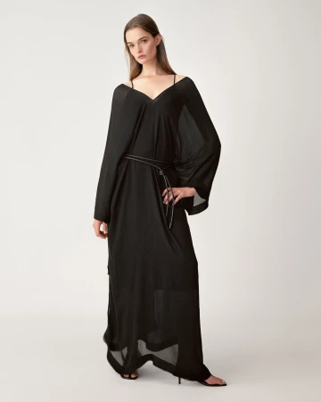 Model wearing a long black sheer dress with a thin belt standing against a seamless white studio background