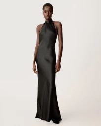 Black woman with short hair wearing a long black halter-neck evening dress against a plain neutral background.