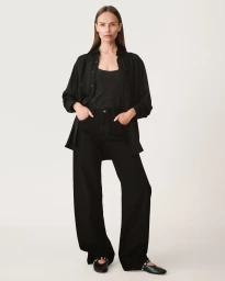 Model wearing black shirt and trousers with hands in pockets against a plain white background