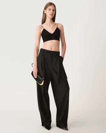 Model wearing a black crop top and wide-leg trousers holding a clutch against a white seamless background