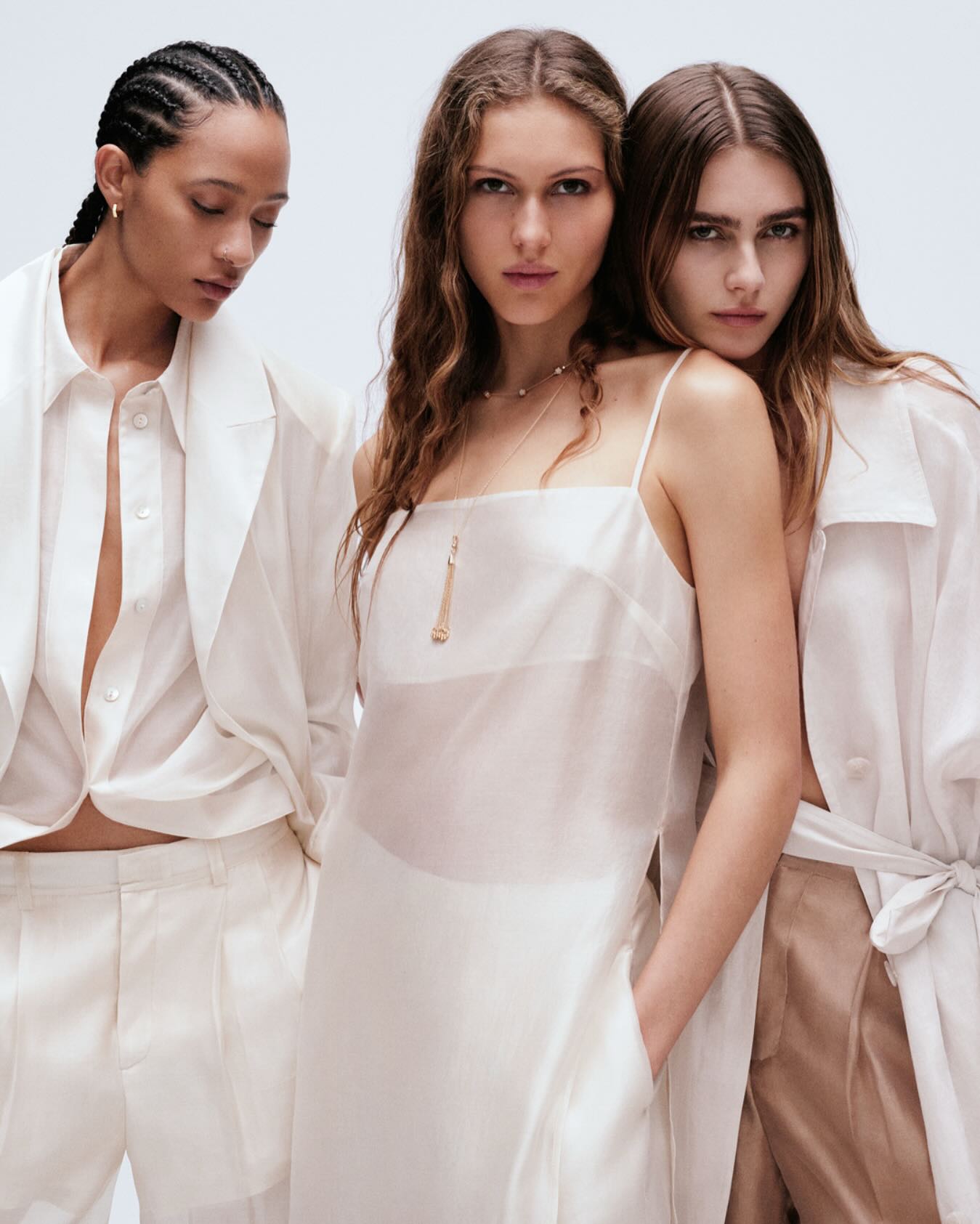 Three female models wearing white and cream apparel posing against a plain white background for an H&M fashion campaign.