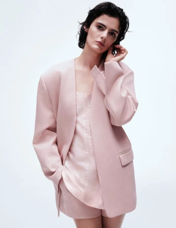 Model wearing a pink oversized blazer and matching top against a clean white seamless studio background.