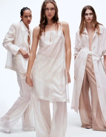 Three female models posing in layered cream and white lightweight apparel against a plain white studio background.