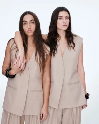 Two models wearing beige sleeveless V-neck vests and matching trousers pose against a clean white background.