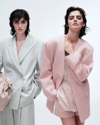 Two models wearing tailored oversized blazers in pale sage green and light pink against a seamless white background.