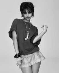Model in dark oversized t-shirt and light mini skirt wearing layered necklaces and bracelets against a grey seamless background