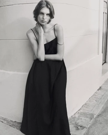 Model in a black slip dress leaning against a curved architectural wall in a monochrome fashion portrait.