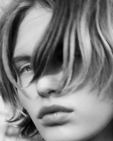 Monochrome close-up portrait of a model with short tousled hair partially covering one eye.