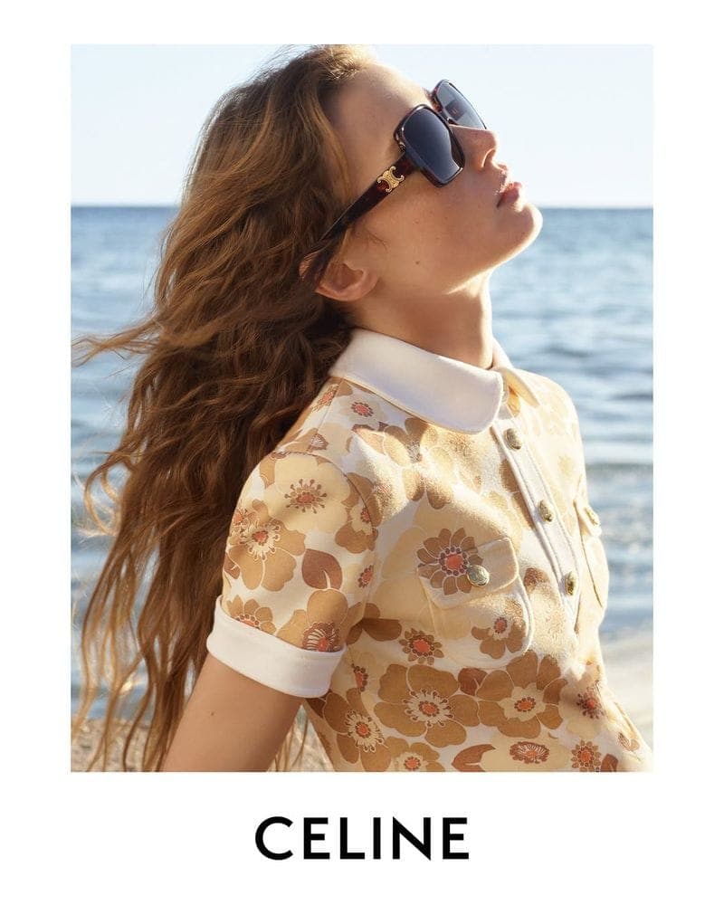 Model in oversized sunglasses wearing a patterned polo top with white collar against an ocean backdrop for Celine