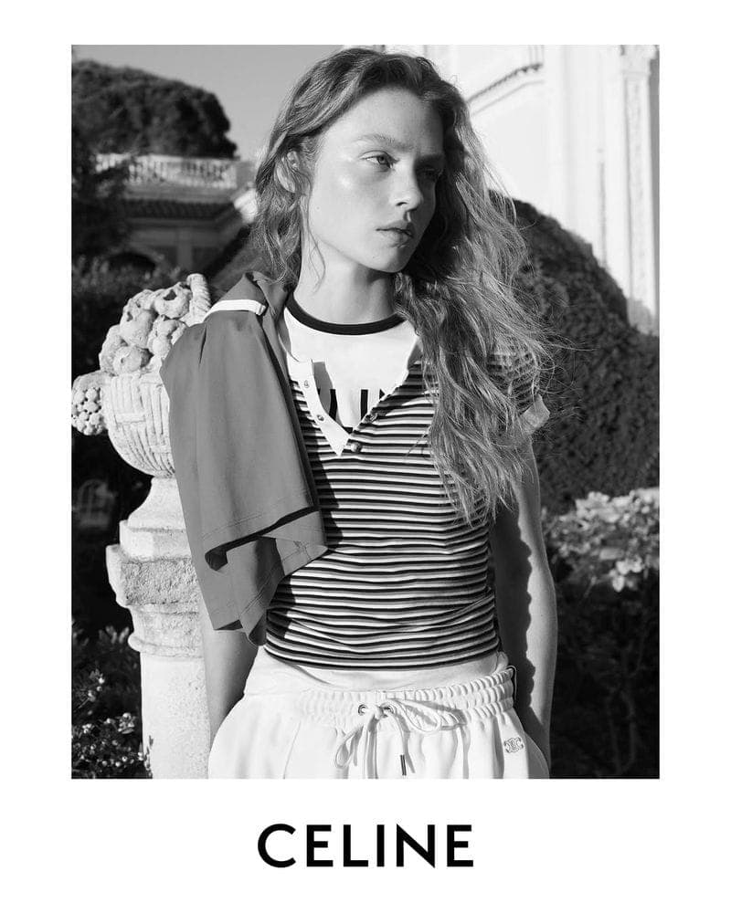 Model in a striped t-shirt and light-colored drawstring trousers standing outdoors near a stone urn for Celine