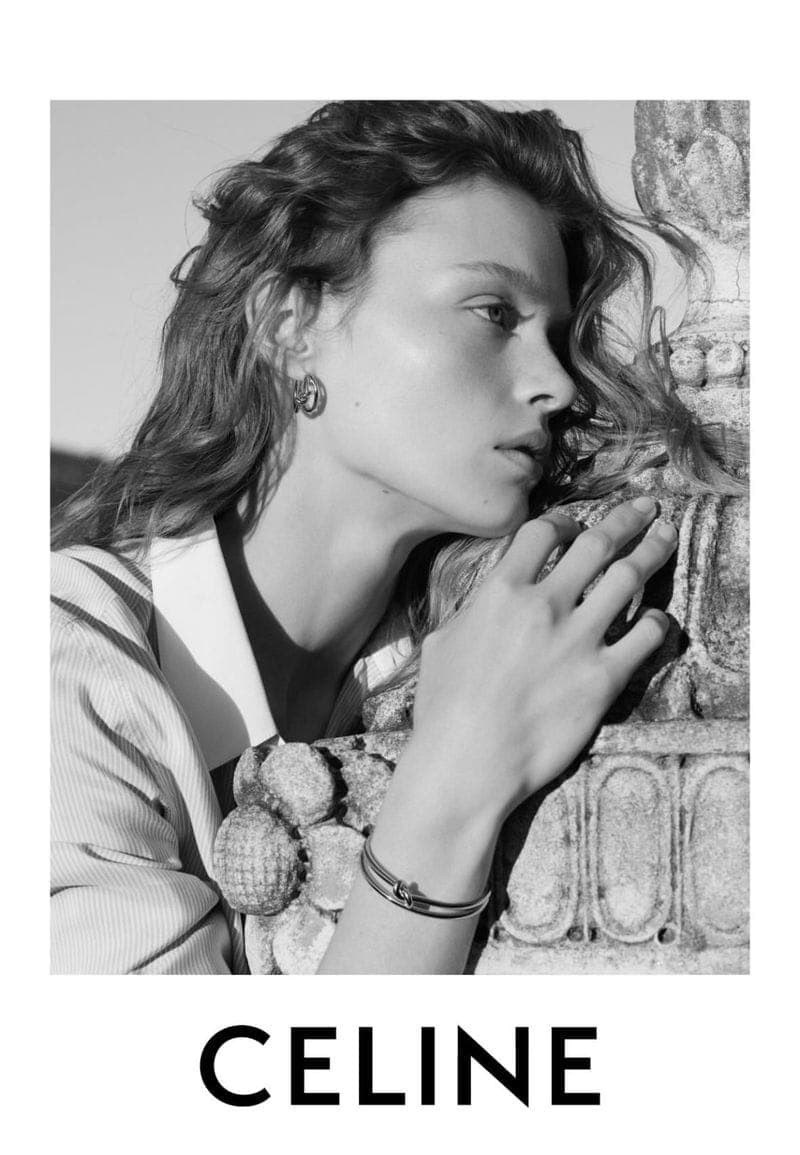 Monochrome portrait of a female model leaning against a carved stone column, wearing jewelry.