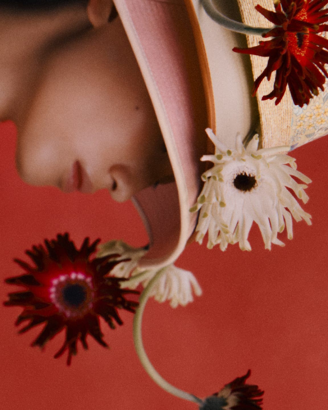 Close-up profile of a model wearing a decorated straw hat adorned with flowers against a solid red background