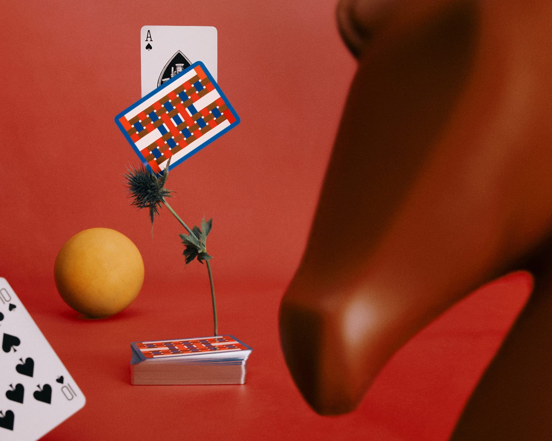 Surreal still life with playing cards, a yellow sphere, and a brown horse sculpture on a red background