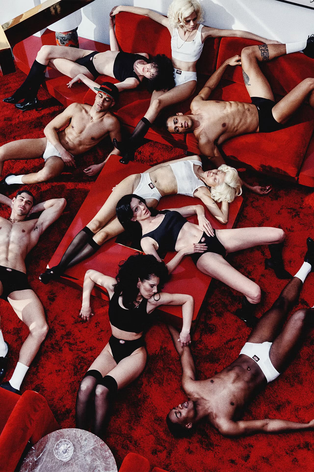 Group of models in undergarments reclining across a plush red carpet and red sofa in a high-angle lifestyle advertising campaign shot.